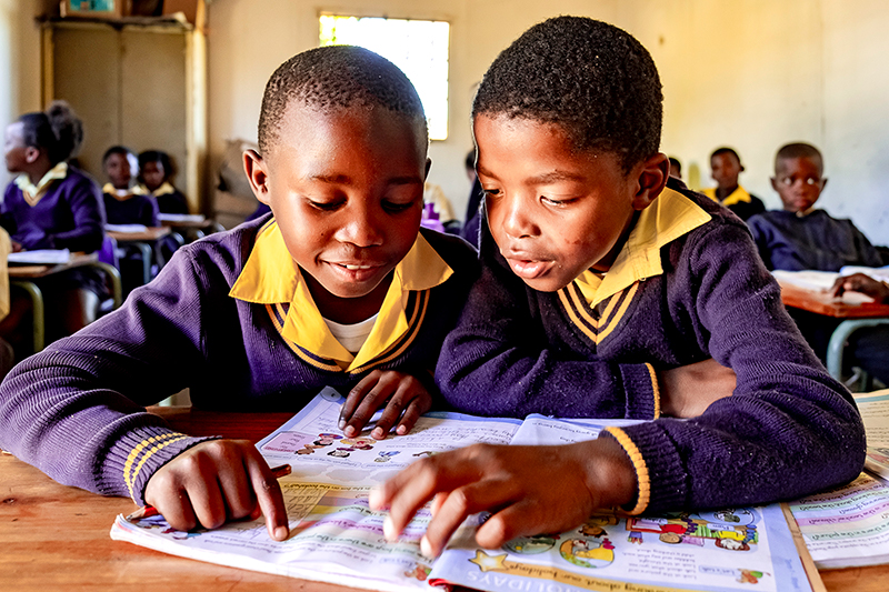 Twee kinderen zitten voorovergebogen en bekijken het lesboek in een Zuid-Afrikaanse klas